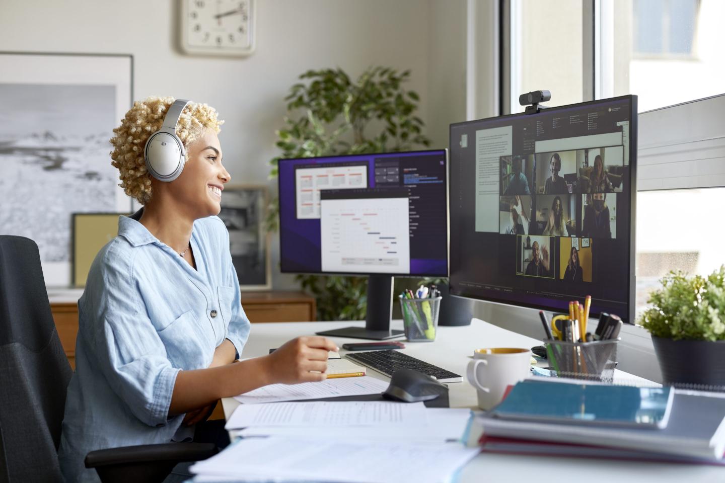 Smiling female professional working at home office wearing wireless headphones.