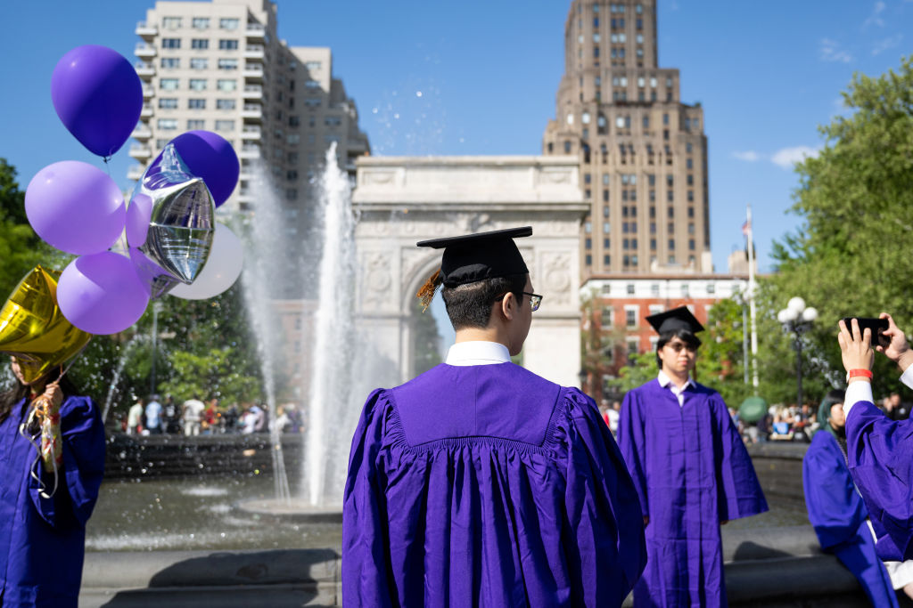 New York University (NYU) graduates take photos wearing caps and gowns in Washington Square Park, as seen in May 2022 in New York City. (Photo by Alexi Rosenfeld/Getty Images)
