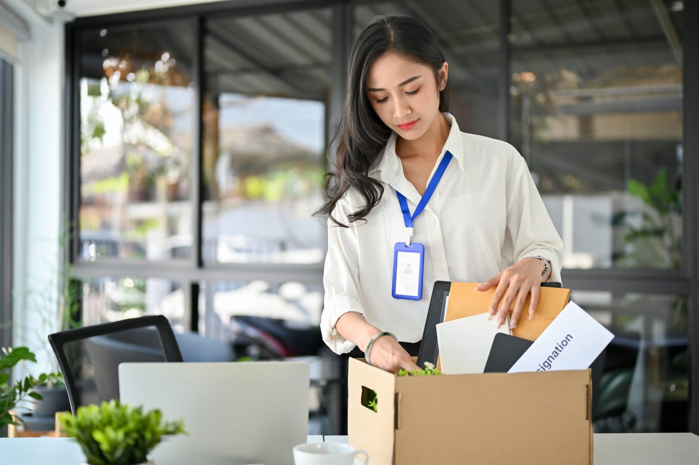 A young businesswoman packs up her workplace possessions into a cardboard box, a signifier that someone is leaving their job.