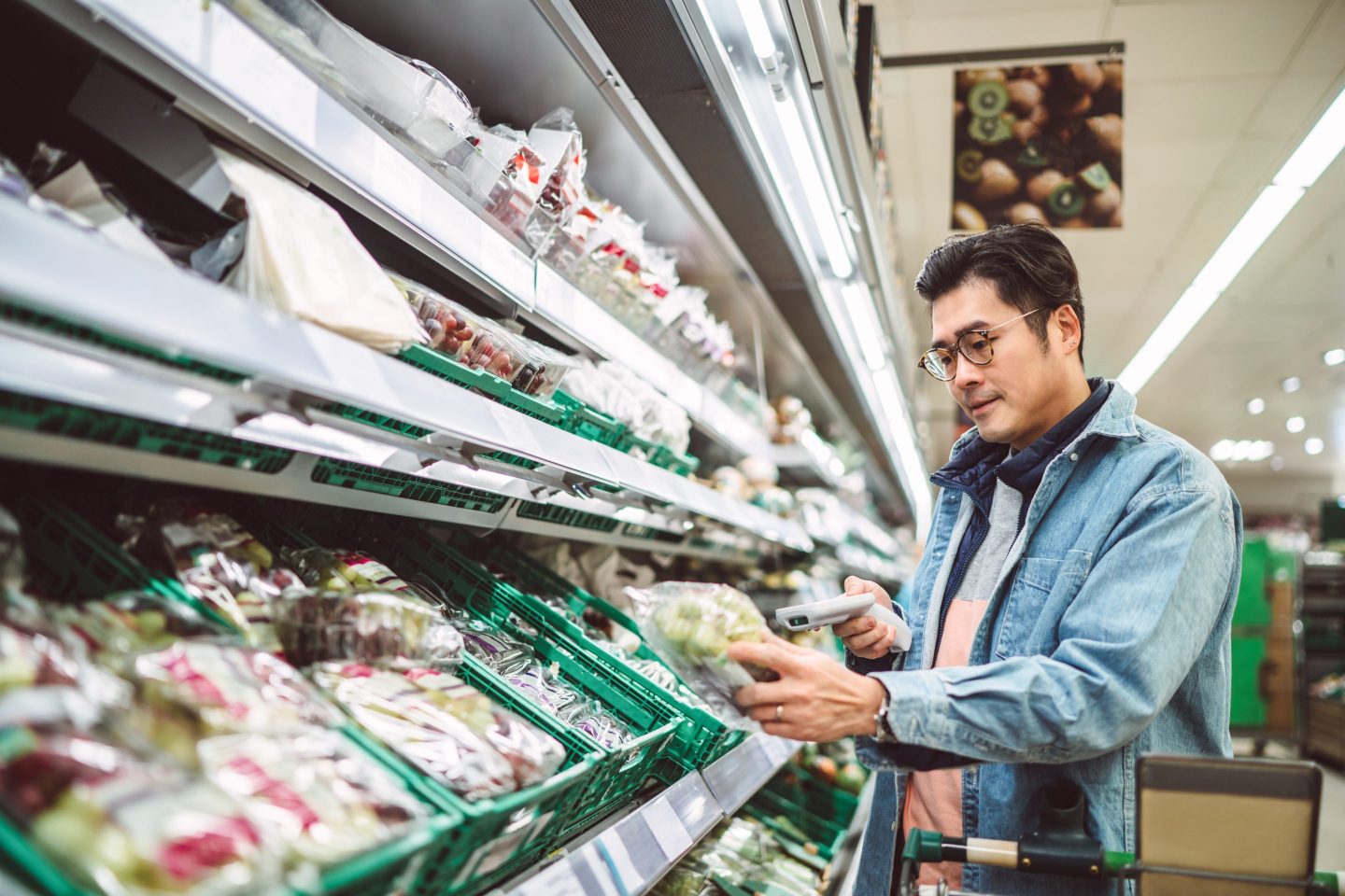 Young handsome man using handheld barcode reader scanning a pack of fresh vegetable while shopping in supermarket