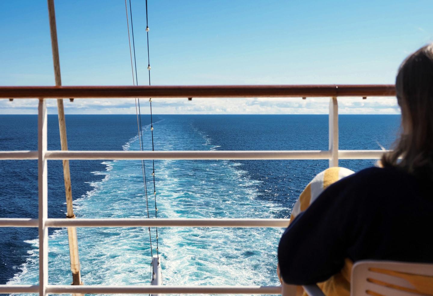 A woman sits on the deck of a cruise ship looking out at the water