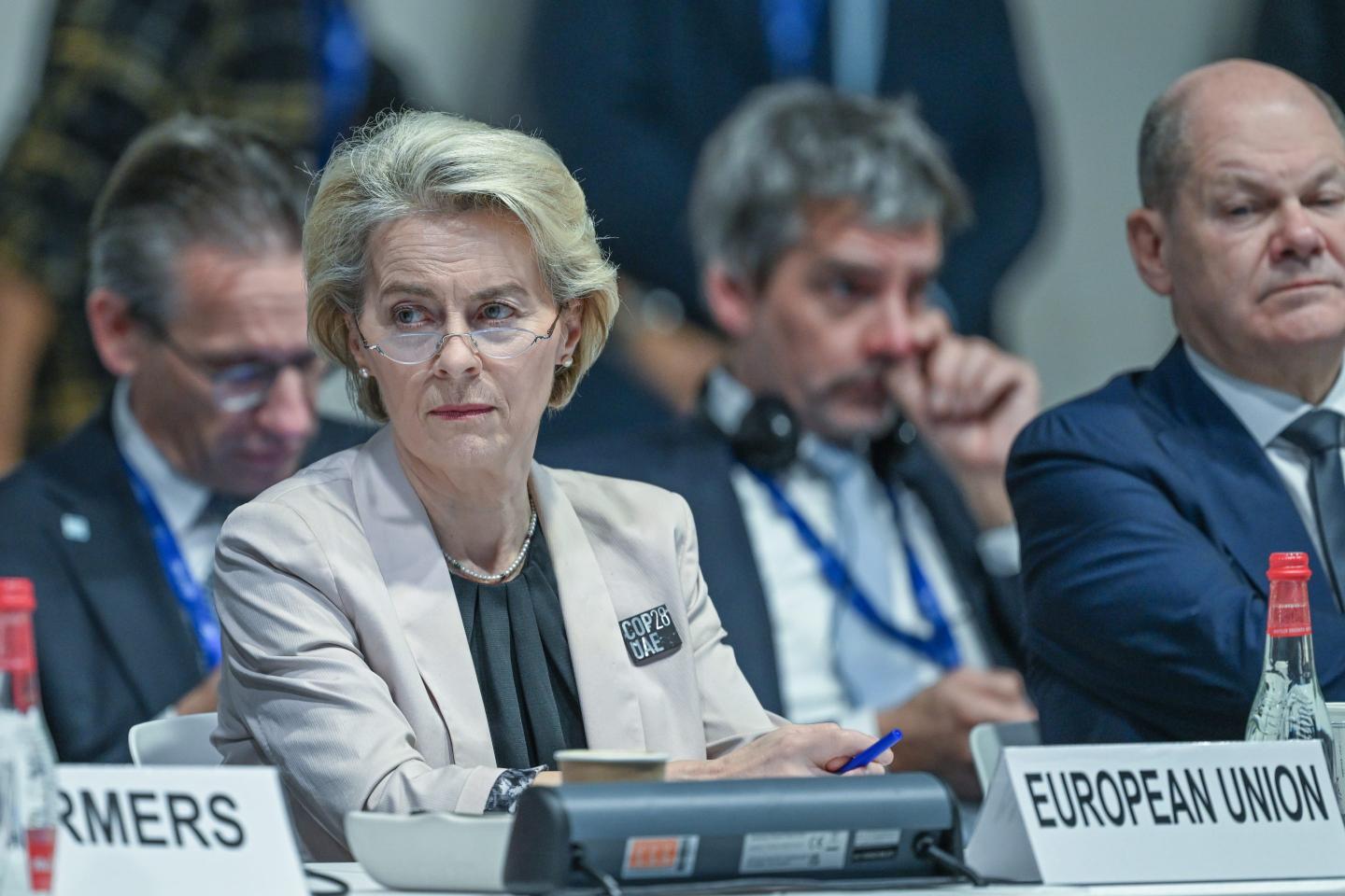 A woman with blonde hair wearing glasses and sitting amongst a group of individuals with a name card in front of her.