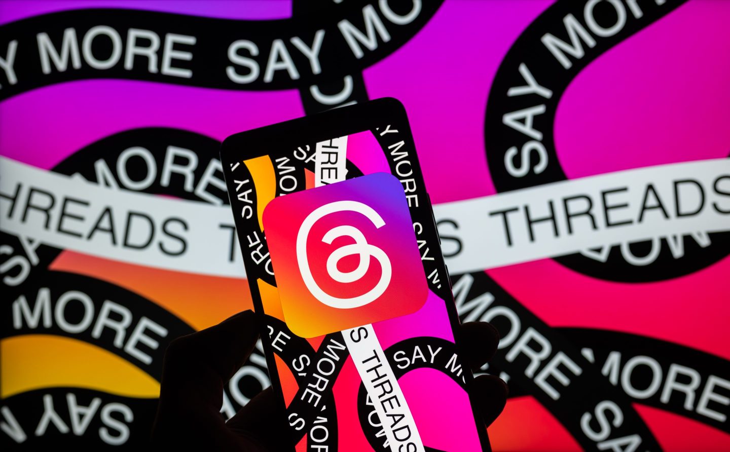 The Meta - Threads logo is being displayed on a smartphone with Threads visible in the background