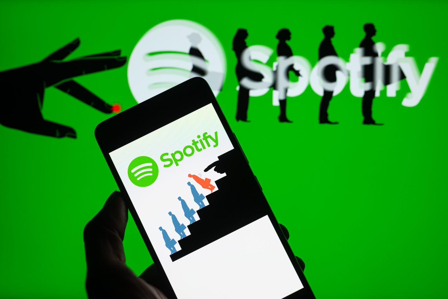 The Spotify logo is being displayed on a smartphone with a Spotify layoff icon in the background