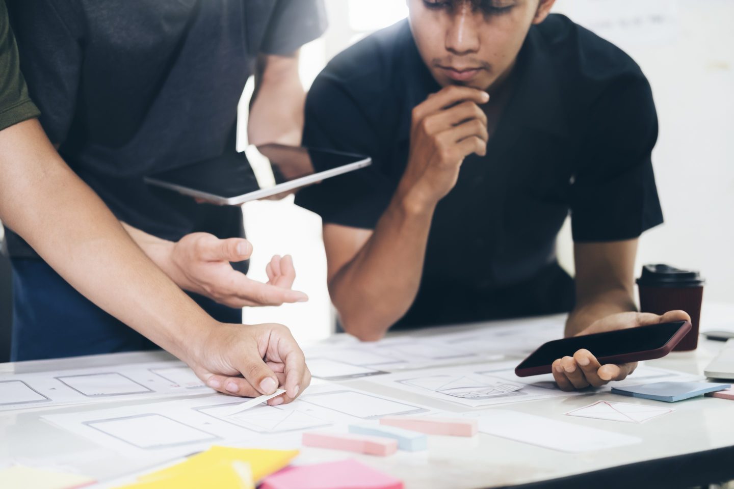 Two designers work on a UX project on a table in front of them.