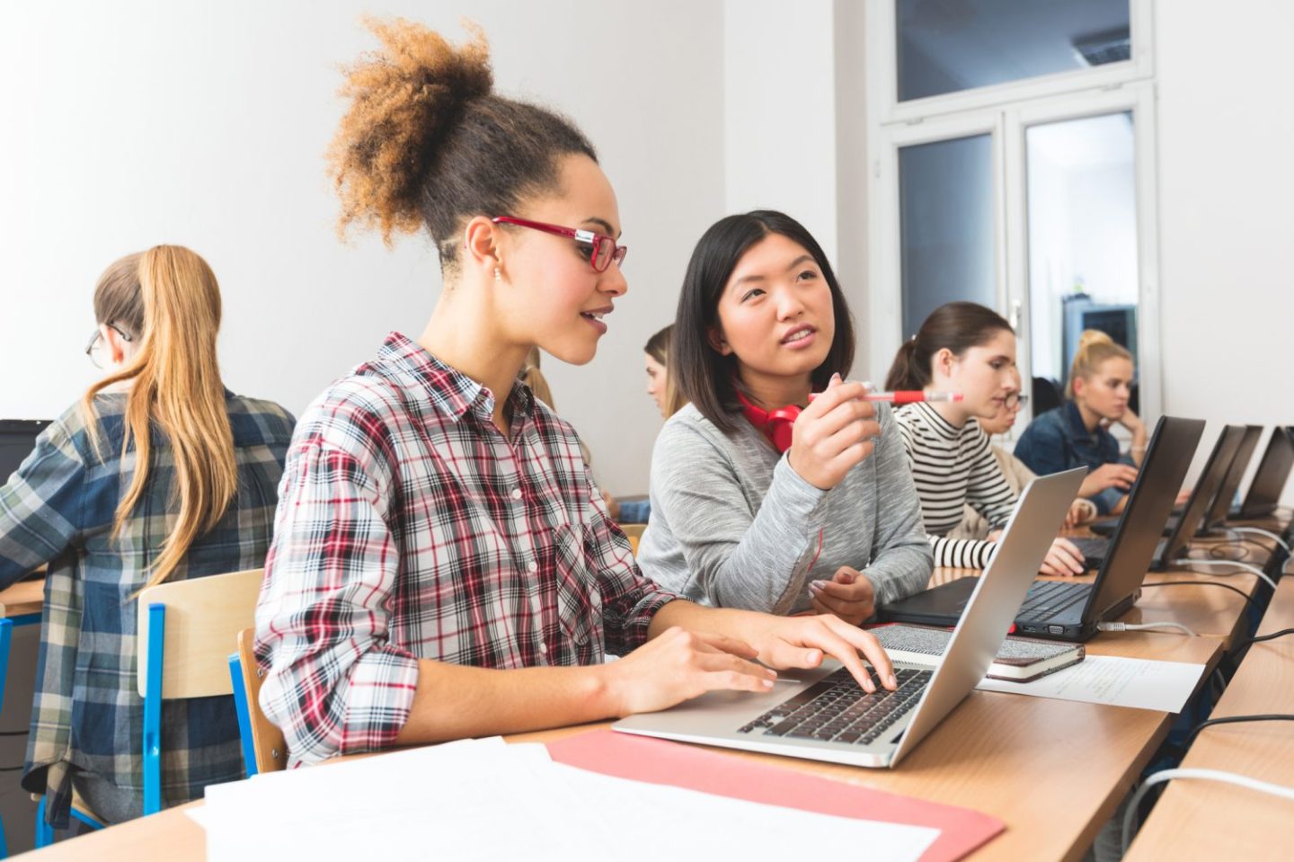 Female students sitting at a long table learning online with laptops