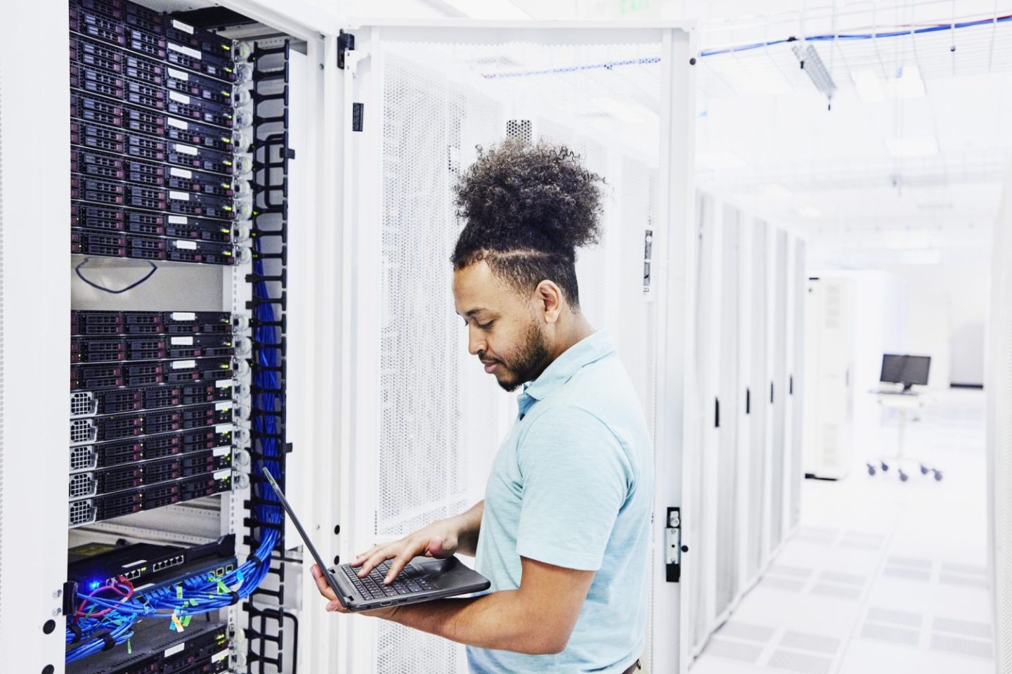 IT technician holding a laptop works next to a computer server