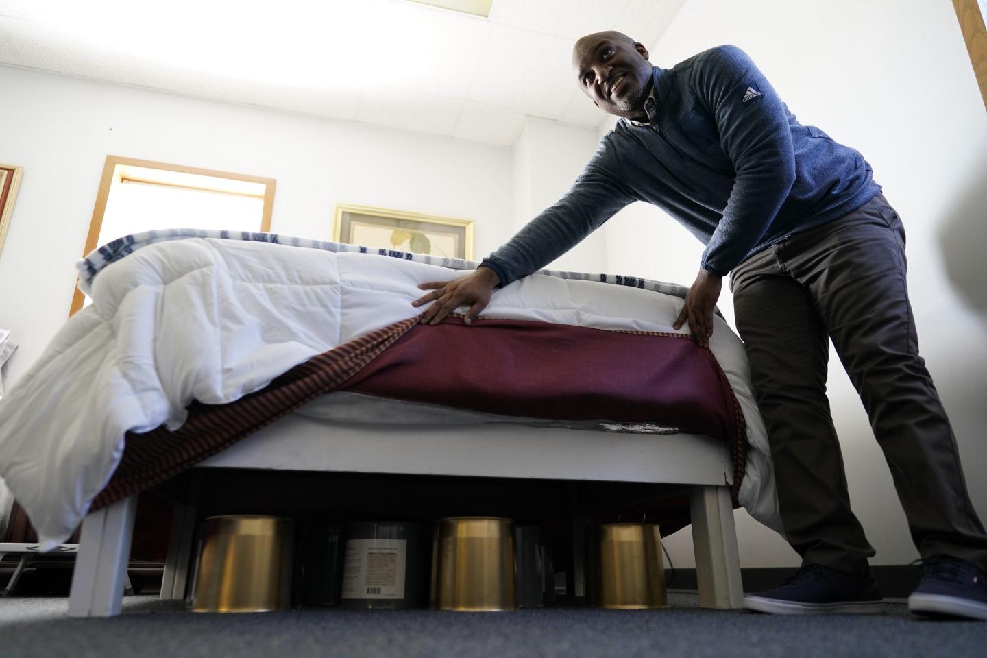 Seth Robinson, a chiropractor who serves as Tesla BioHealing's medical director, lifts bed skirts to show "biohealers" — canisters that the company claims exude "life force energy," or biophotons, at the Tesla BioHealing & MedBed Center, in Milford, Del., on Oct. 3, 2023. According to QAnon adherents, medbeds were developed by the military (in some versions, using alien technology) and are already in use by the world’s richest and most powerful families.