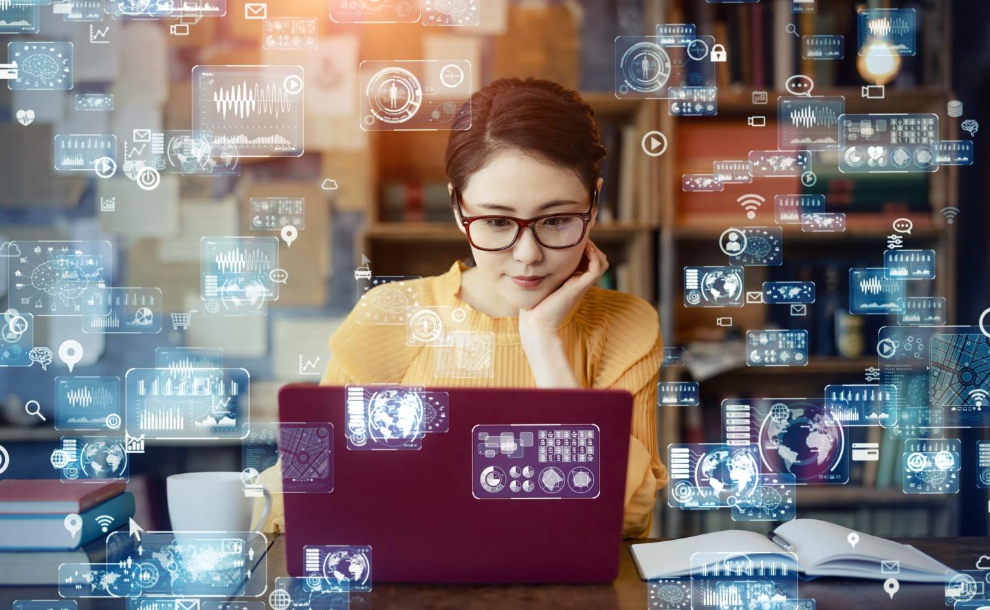 Woman works on a laptop with technology holograms flying around her.