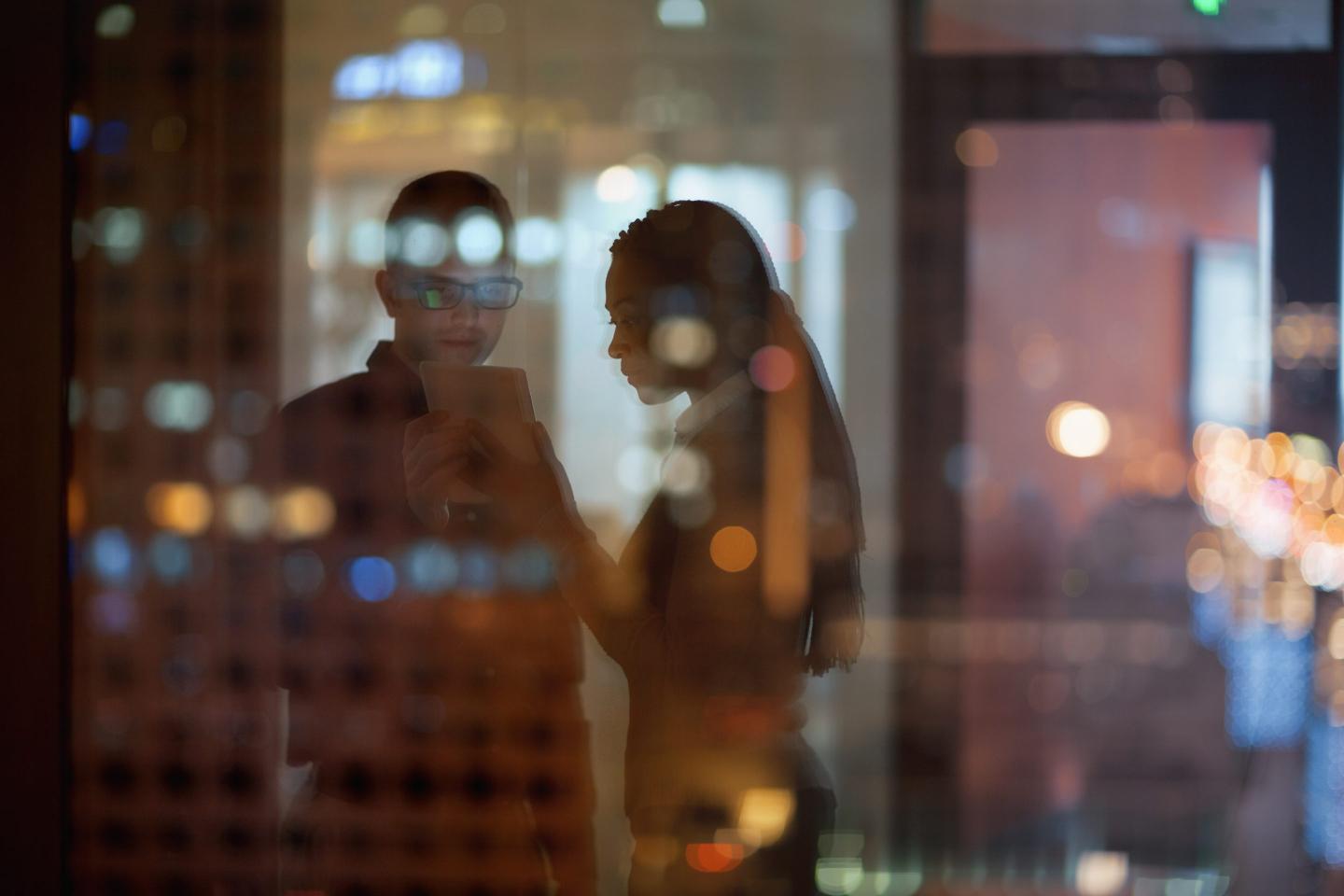 Coworkers looking at tablet in office at night.