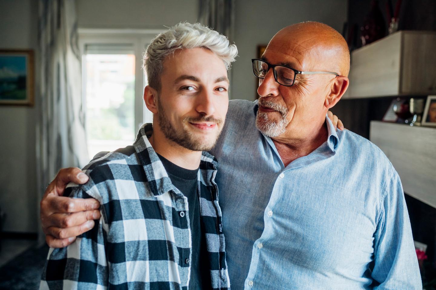 Father with arm around looking at son while standing at home.