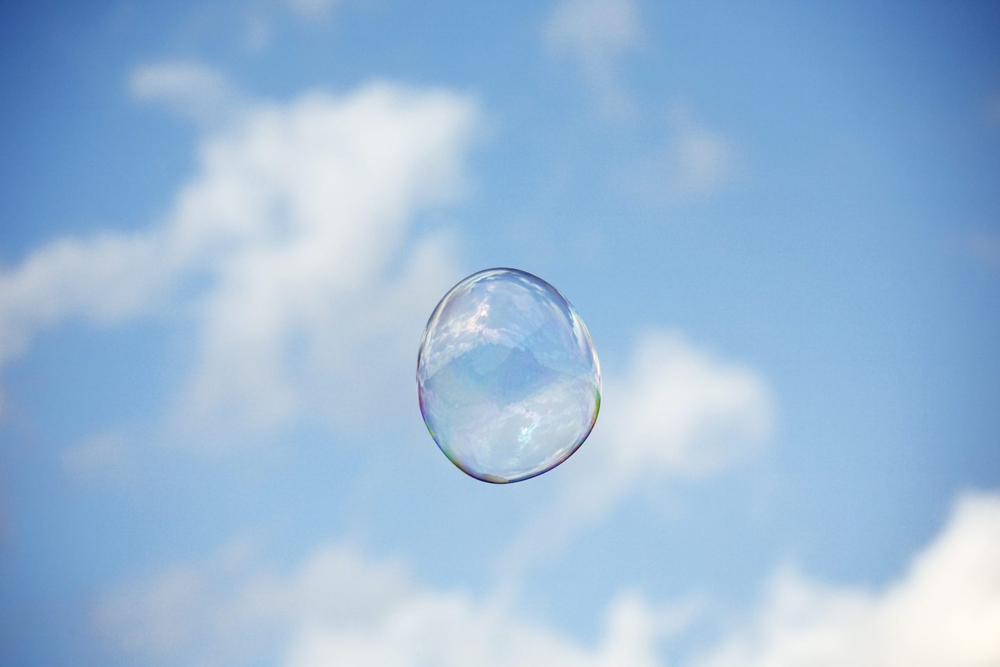 A single bubble floats in a blue sky.