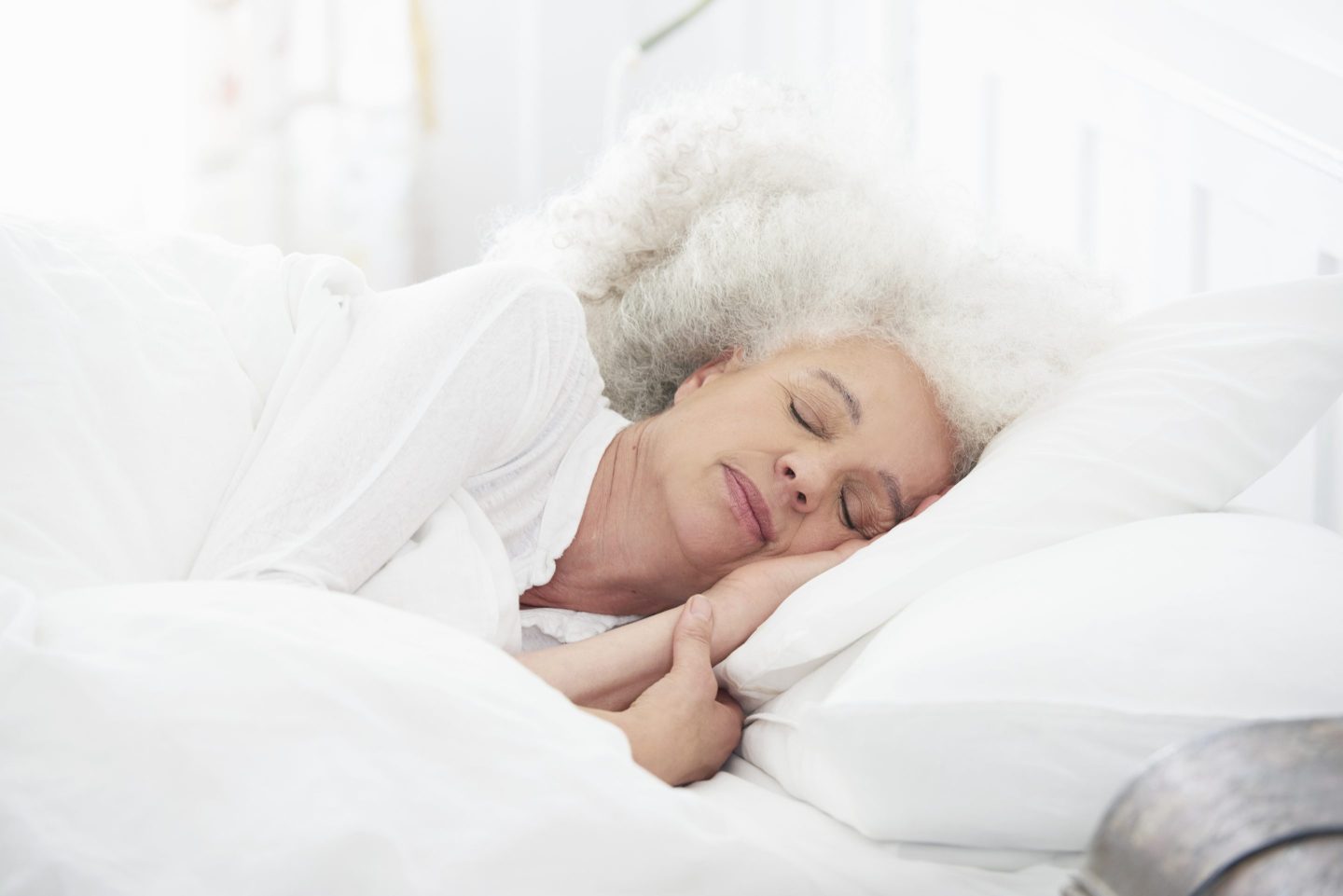 Senior woman lying in white bed.