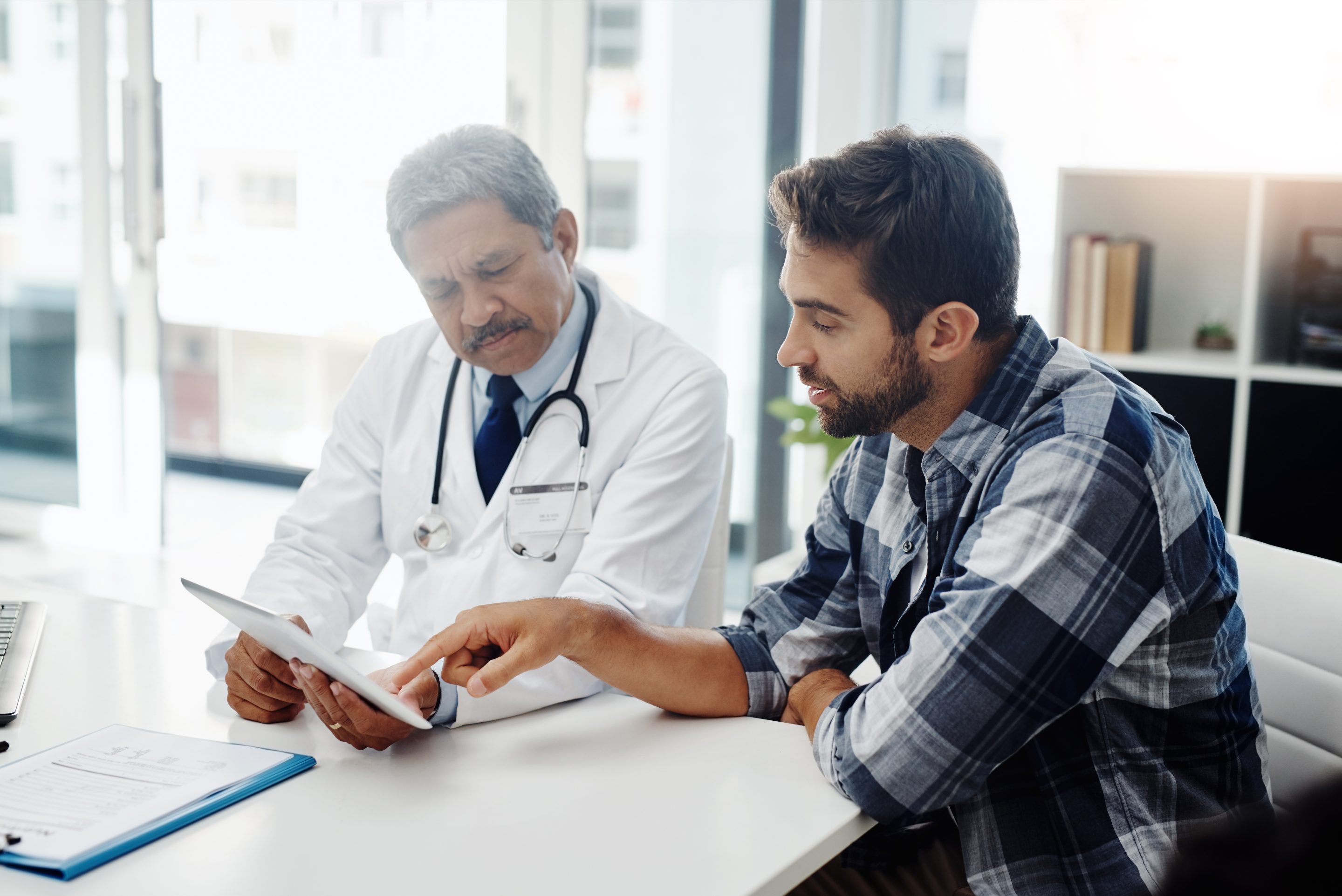 Stock image of a male doctor and male patient having a discussion in the doctor's office.