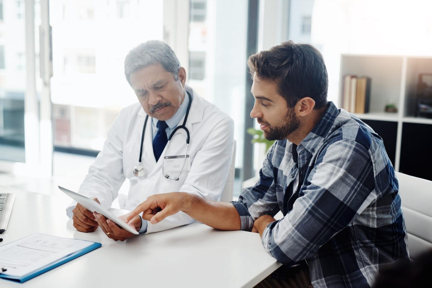 Stock image of a male doctor and male patient having a discussion in the doctor's office.