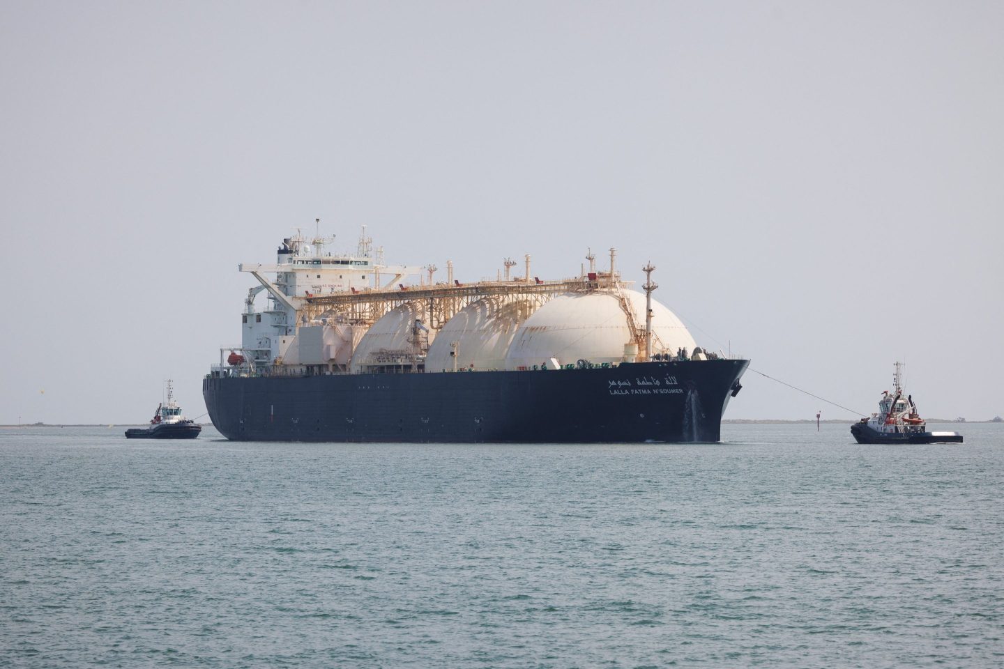 A large tanker boat on the sea surrounded by two smaller boats.
