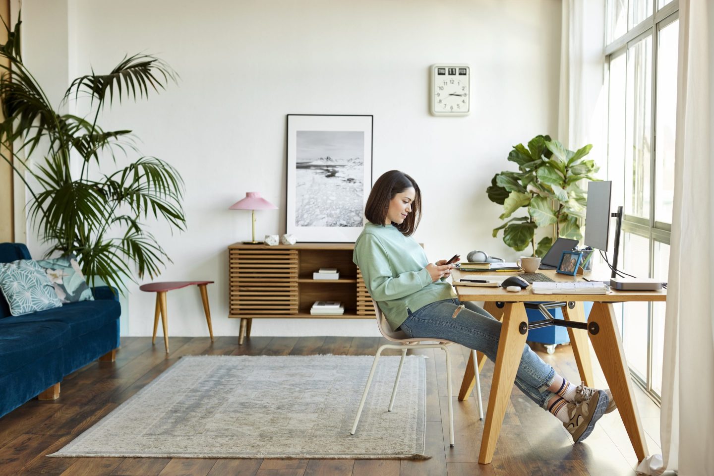 Relaxed female professional using mobile phone at home. Entrepreneur is sitting with legs crossed at table. Businesswoman is text messaging.
