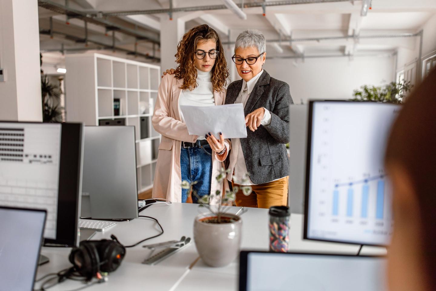 Two women, one older and one younger, converse together in an office.