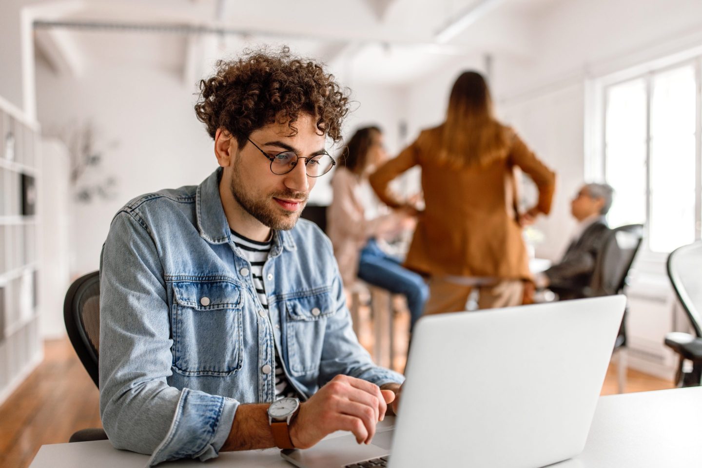 Young man in office ignoring chatting peers.