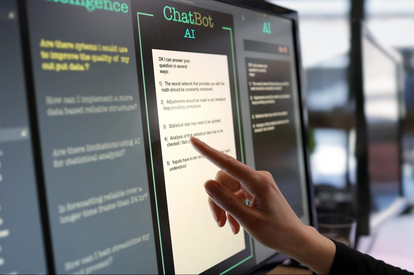 A woman’s hand is asking an AI chatbot questions on a touchscreen monitor.