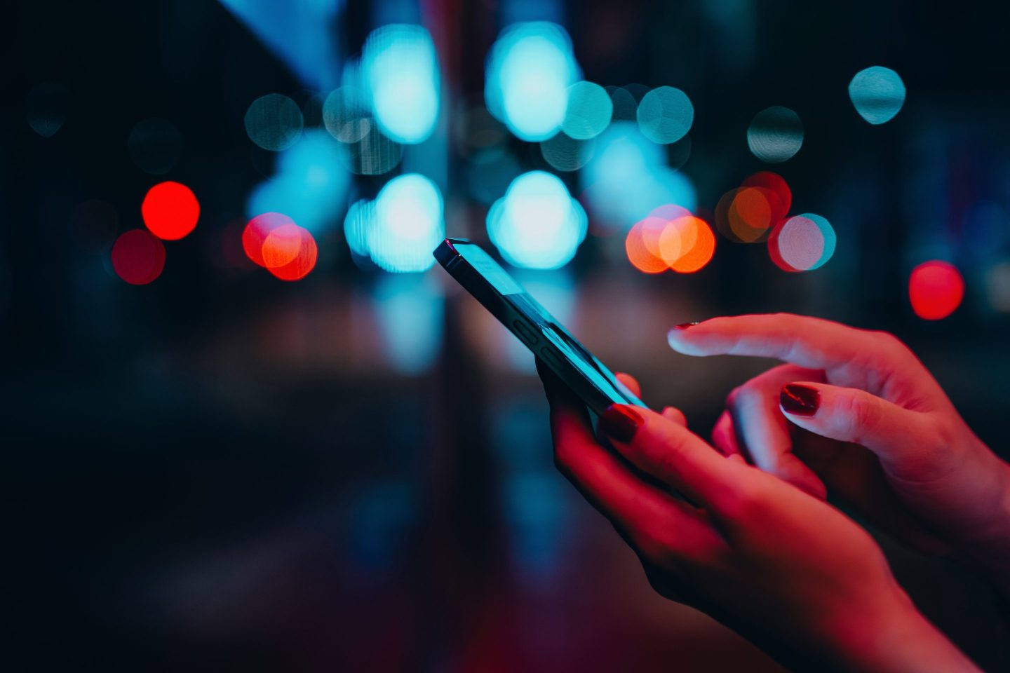 Young woman networking with social media on smartphone in city street at night. Defocus street lights in background. Close up of woman checking social media on smartphone in the city. People engaging in networking with technology. Lifestyle and technology