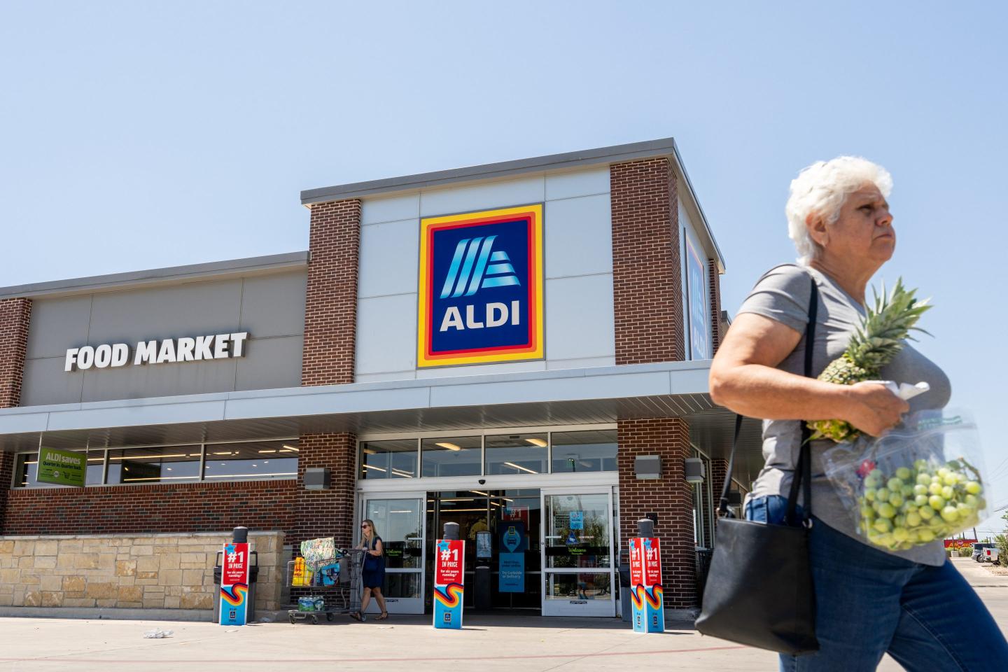 A customer walks out of an Aldi supermarket holding groceries in her hands.