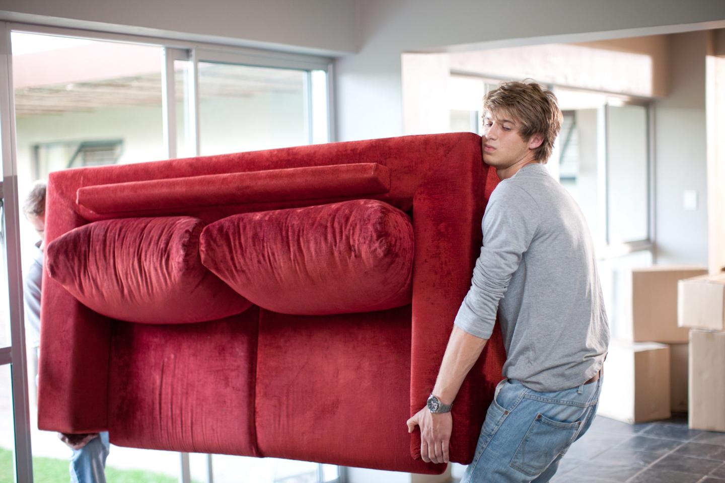 Two people carrying a red couch