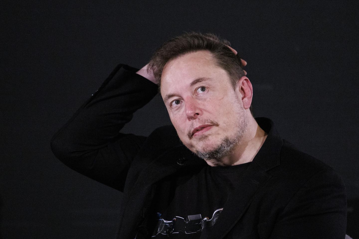 X CEO Elon Musk with hand on head, contemplative