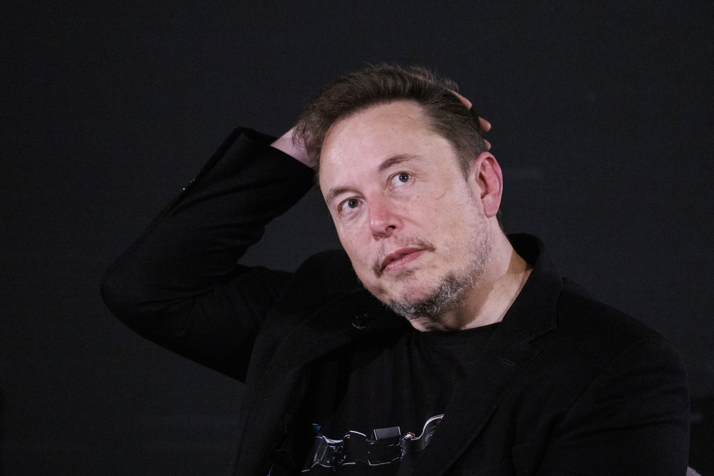 X CEO Elon Musk with hand on head, contemplative
