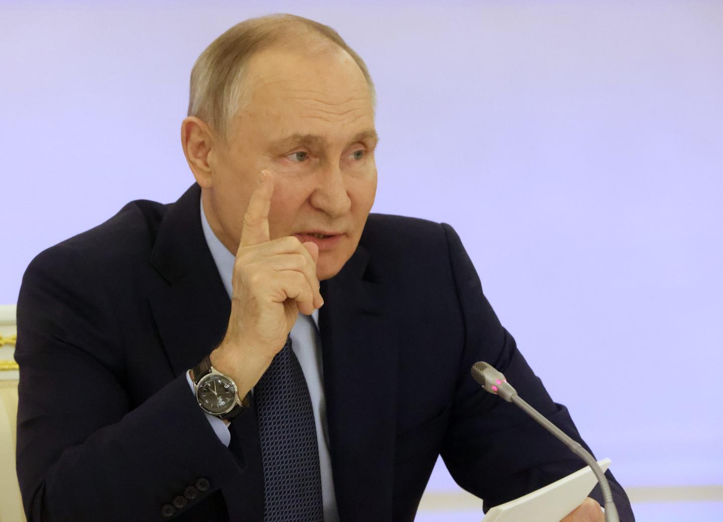 vladimir putin talking with his right hand raised in the air