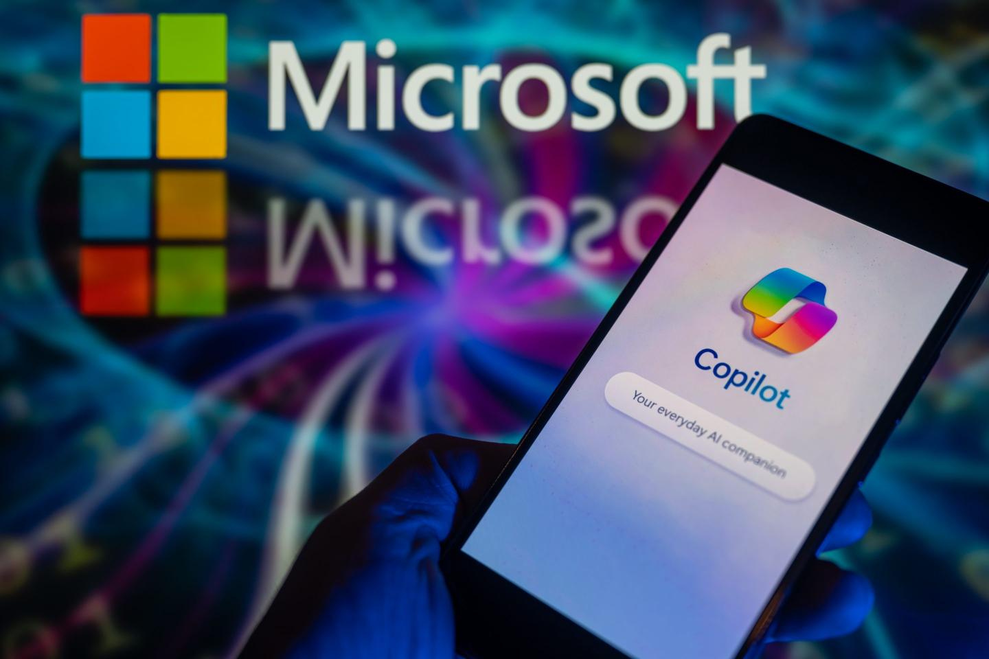 The Microsoft Copilot app is being displayed on a smartphone, with the Microsoft logo visible in the background