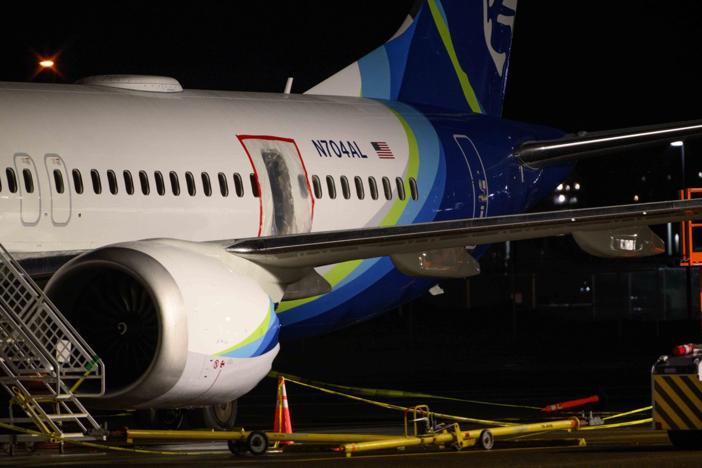 A plastic sheet covers an area of the fuselage of the Alaska Airlines N704AL Boeing 737 MAX 9 aircraft outside a hangar