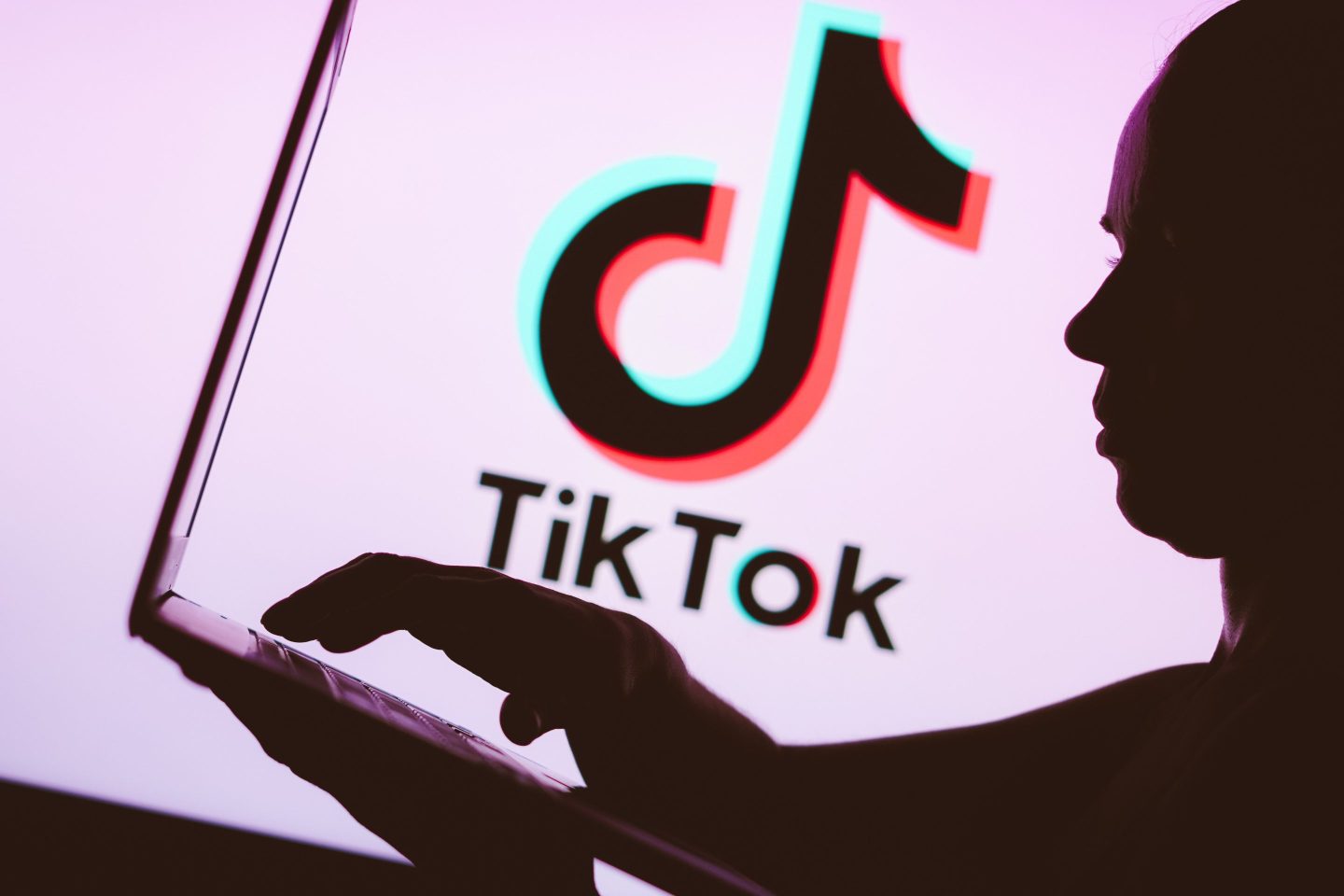 TikTok logo is seen in the background of a silhouette of a person using a notebook.