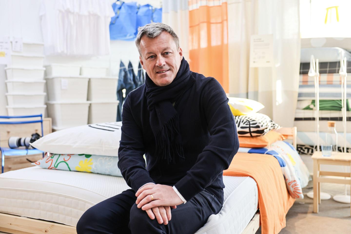 a person sitting on a bed with miscellaneous furniture items in the background