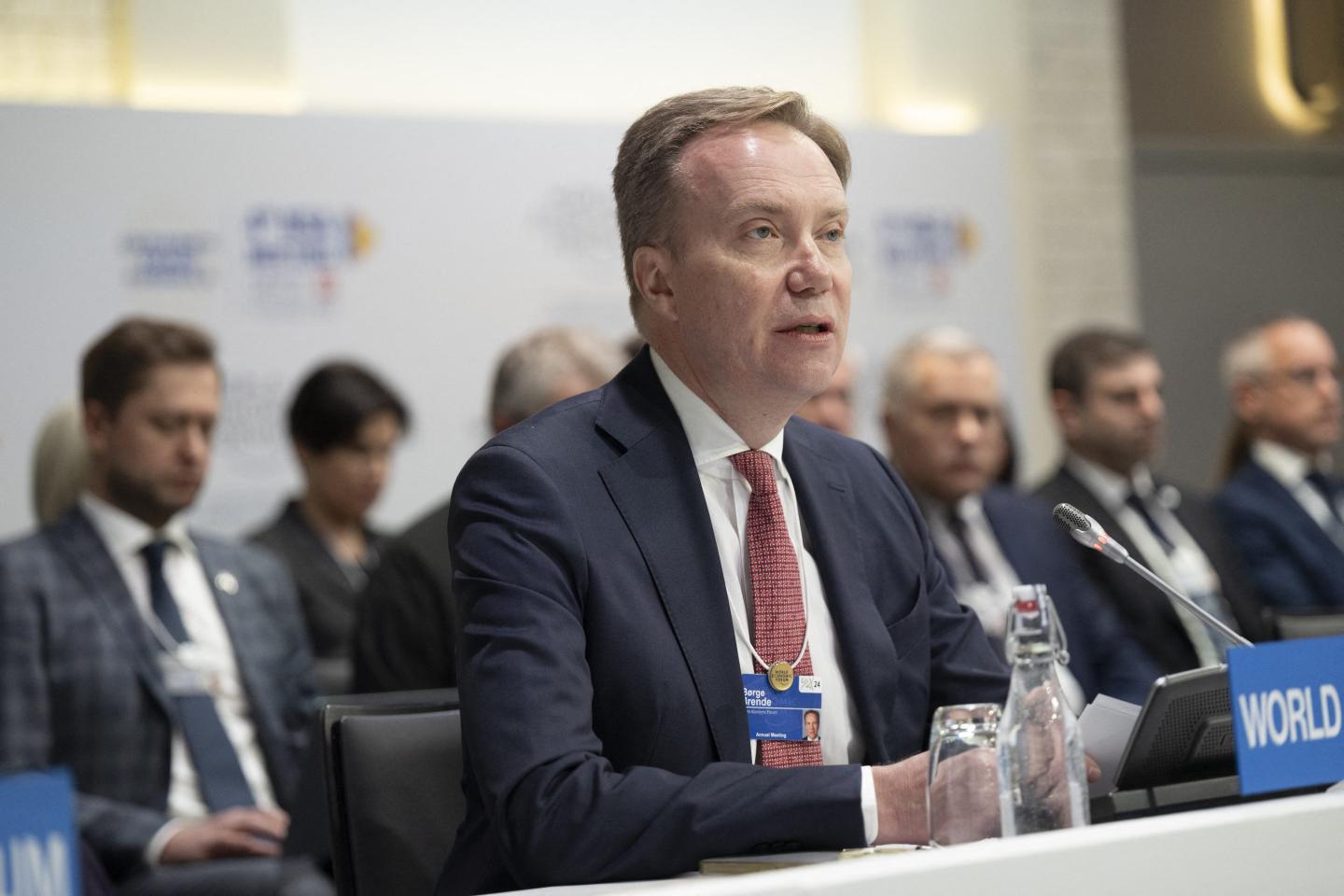 A man wearing a navy suit with a red tie among a group of panelists.