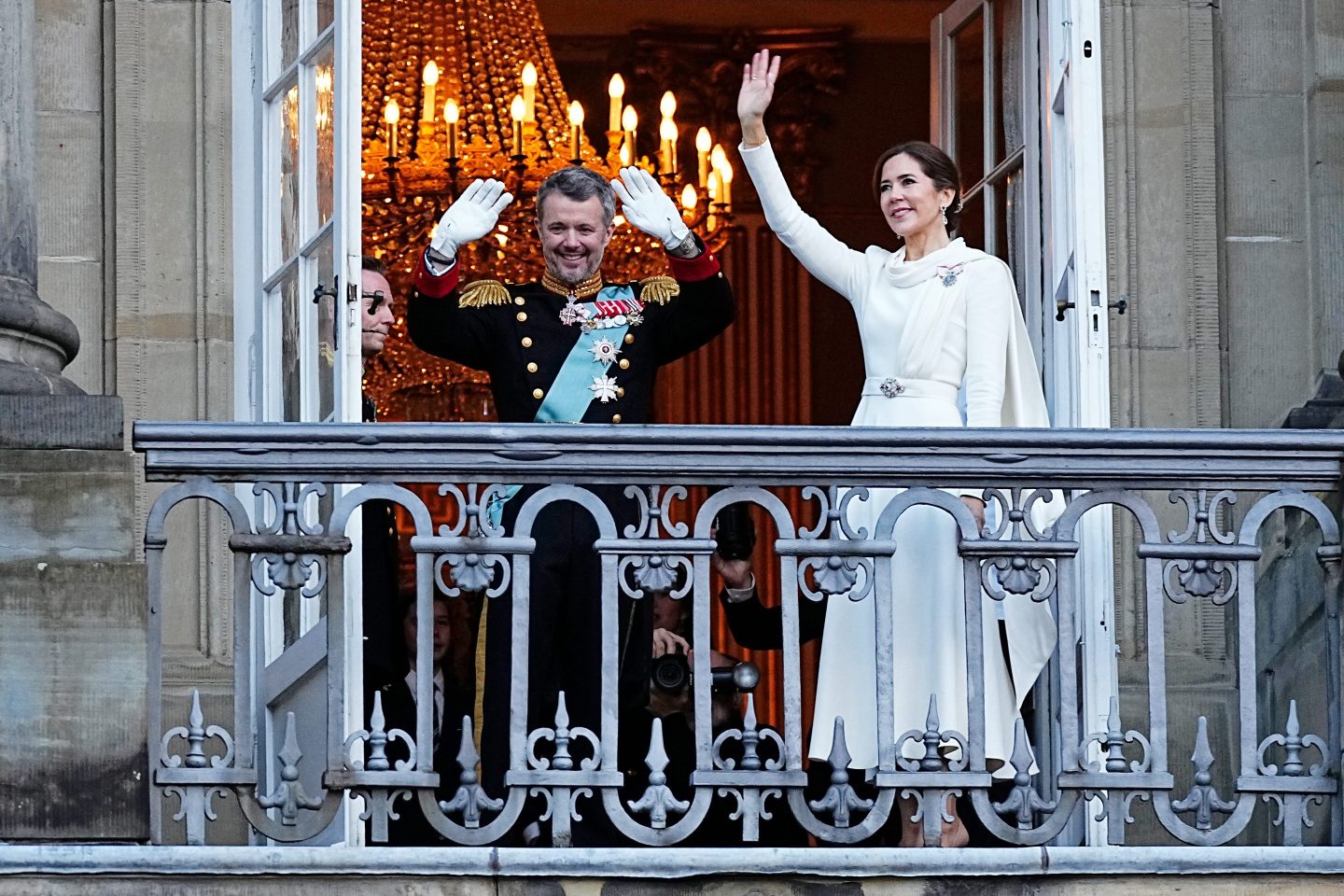 King Frederik X and Queen Mary of Denmark wave from a balcony.
