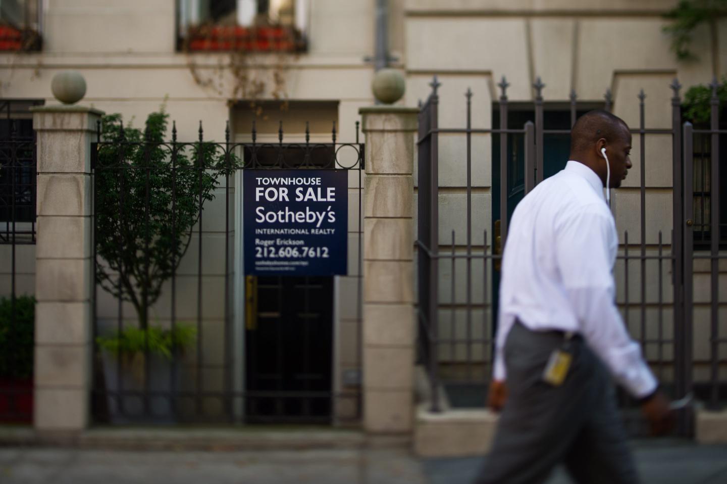 Man walking past a New York building with a sign that says Townhouse for sale.