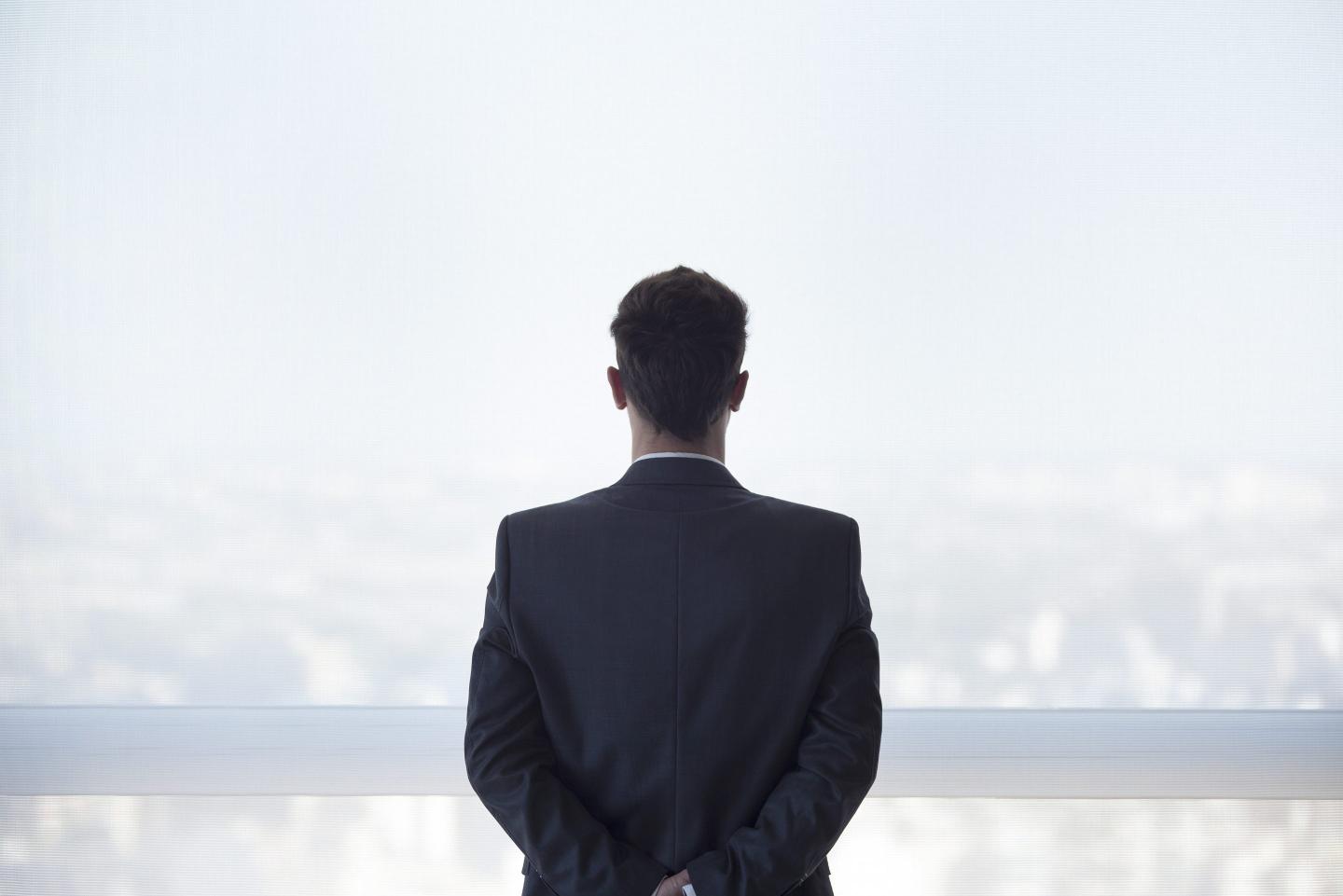 Businessman looking out high rise window at view of city below, rear view