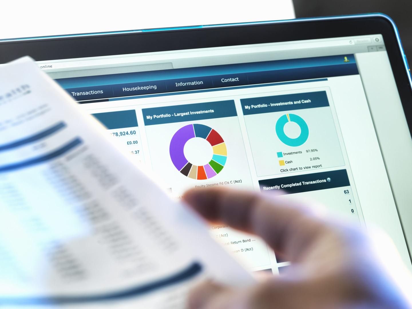 Investor checking performance of financial portfolio online whilst reviewing investment statement
