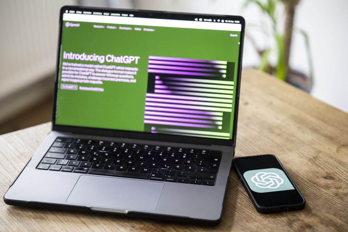 A laptop displays ChatGPT's website with a phone next to with OpenAI's logo.