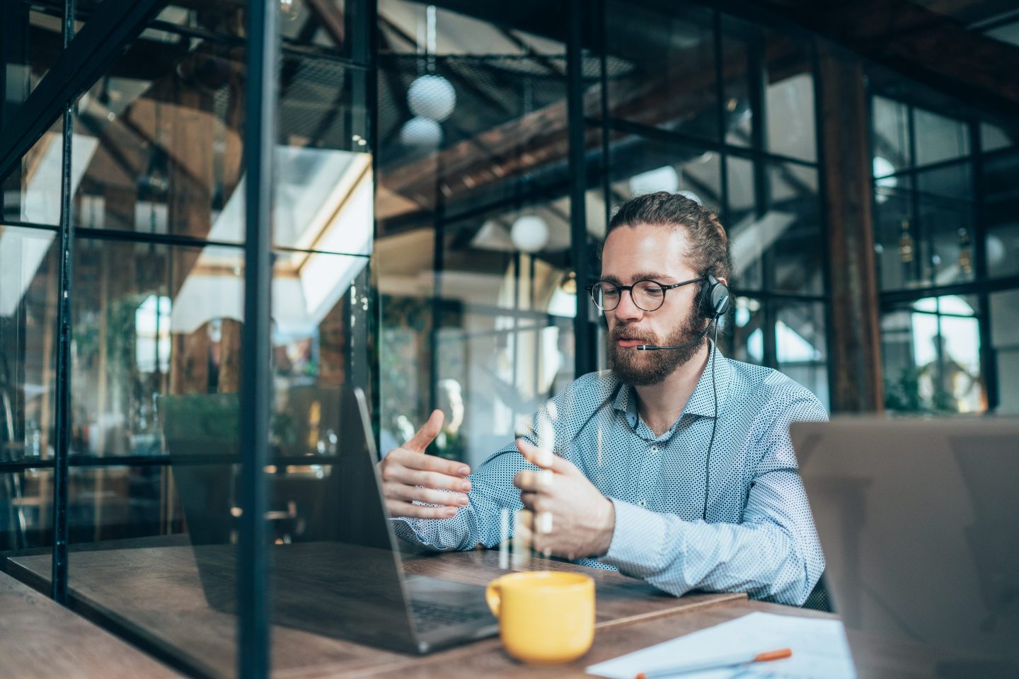 Young businessman with a headset on in a modern office talks to a laptop video call