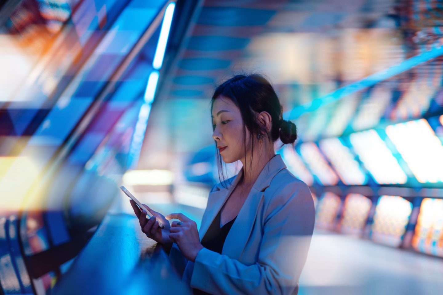 Young Asian business woman holding smartphone with a computer generated background with futuristic flashy lights.