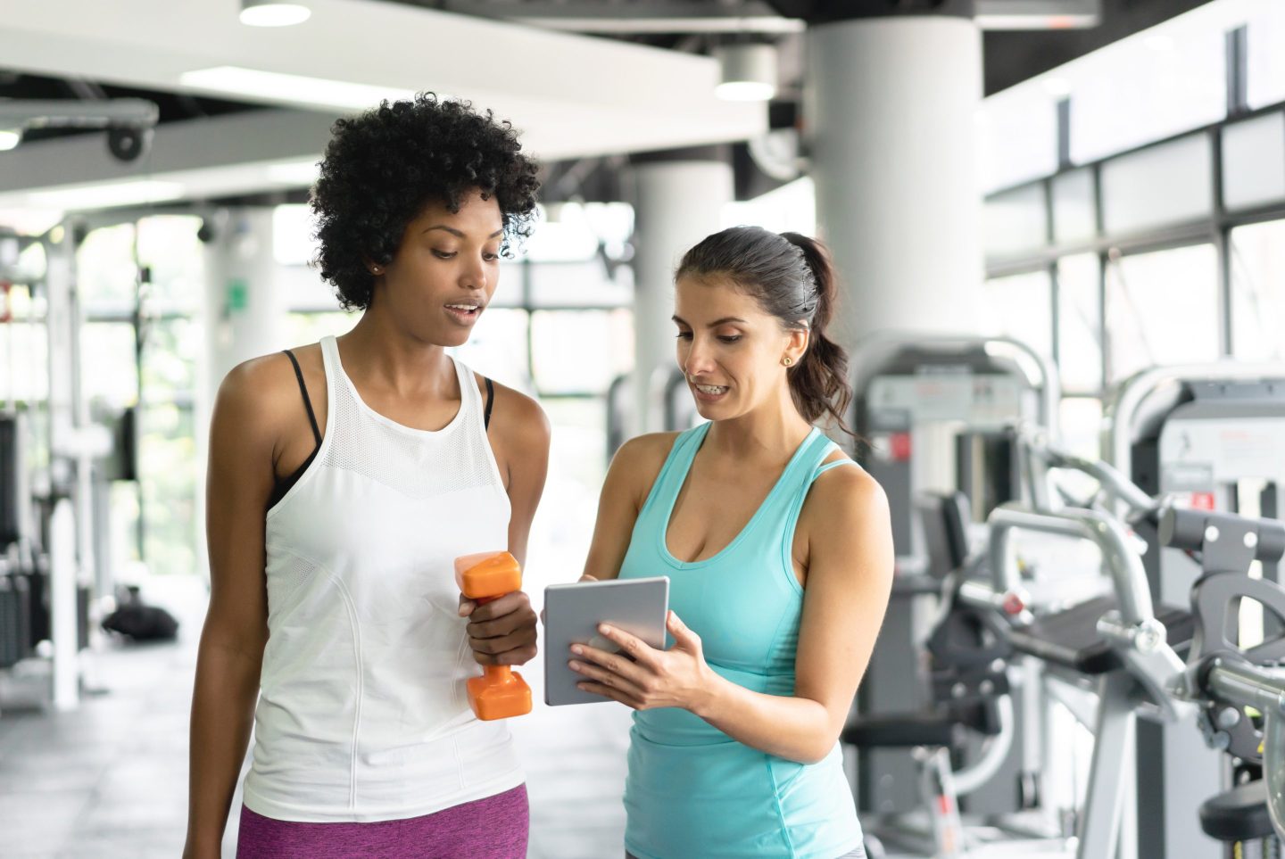 Female personal trainer showing black woman the routine on tablet while talking