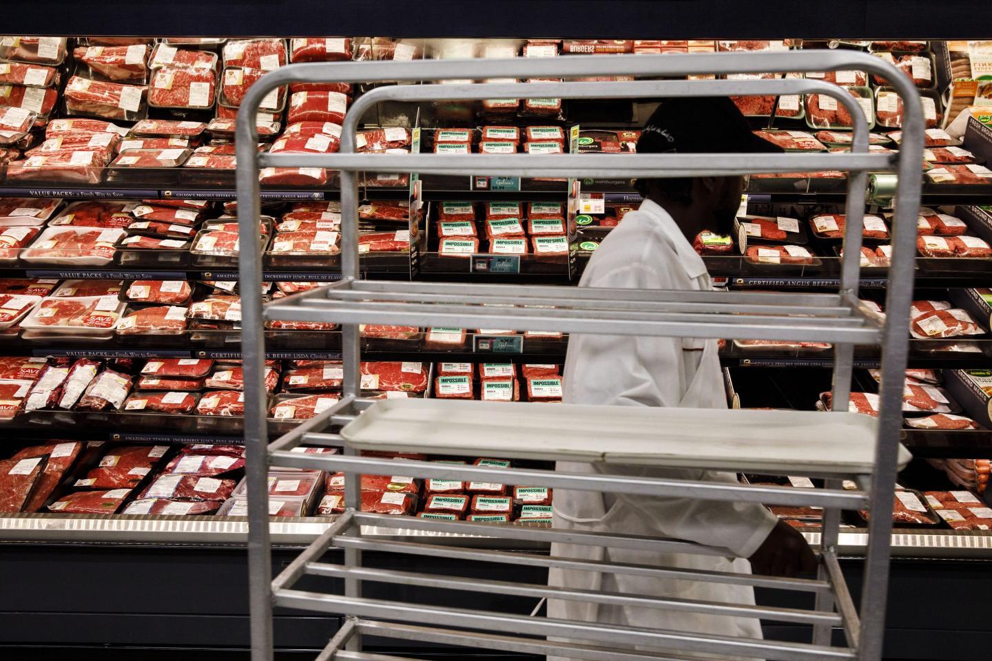 A grocery worker stocks the refrigerated shelves with meat and plant-based meat.