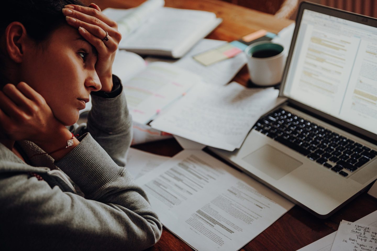 Young woman looking stressed out as she works with papers and her laptop
