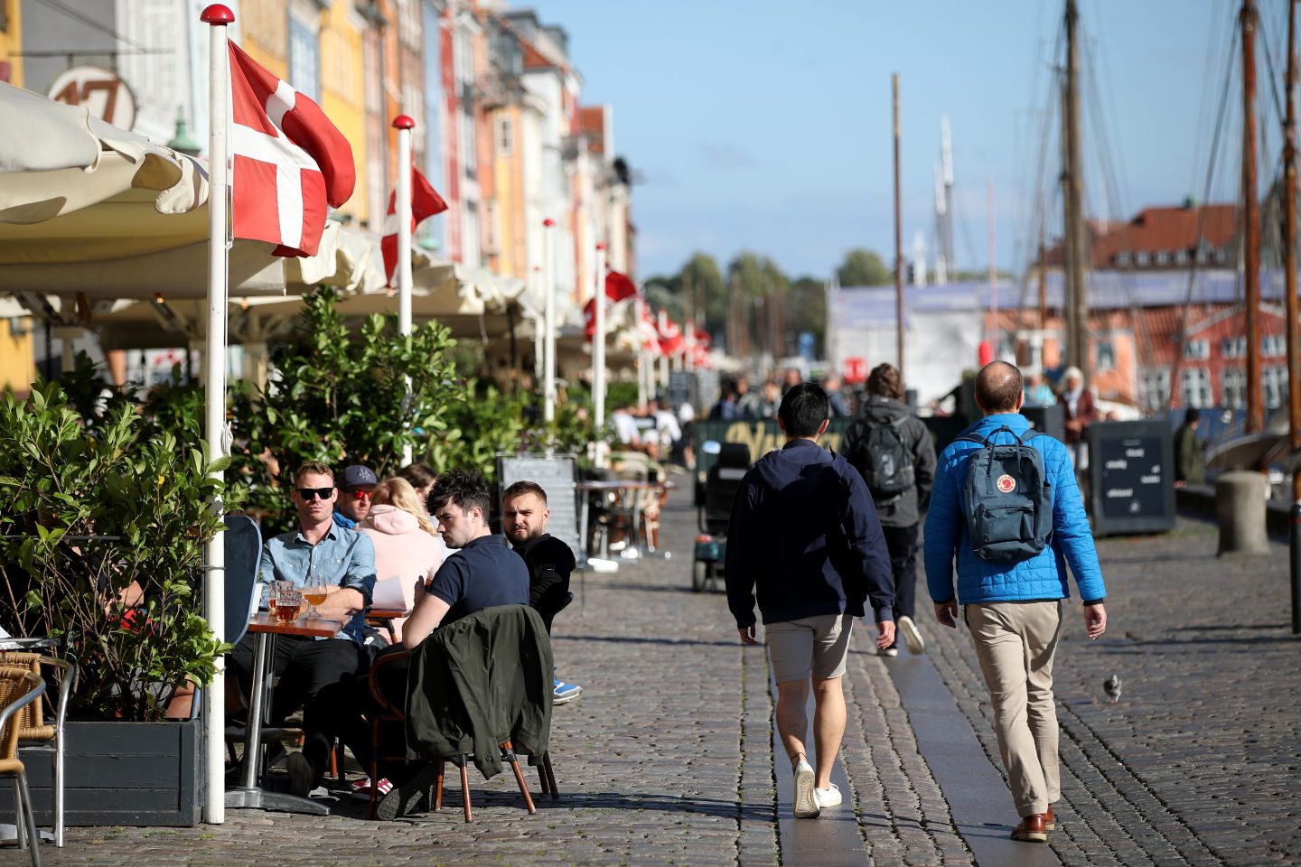 People sit and enjoy drinks in the sunshine at Nyhavn, a waterfront, canal and entertainment district in Copenhagen, Denmark