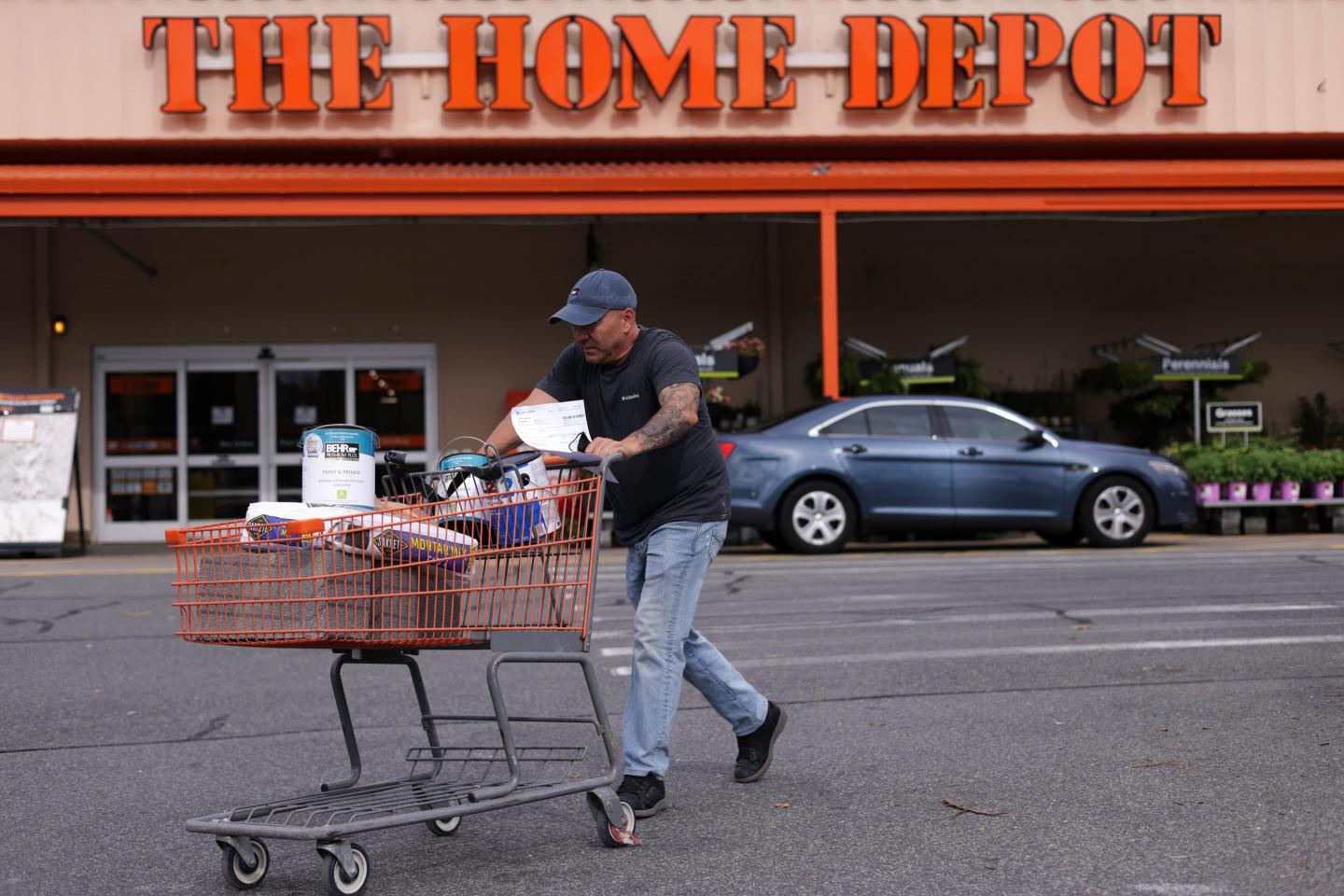 A man pushes a grocery cart across a Home Depot parking lot.