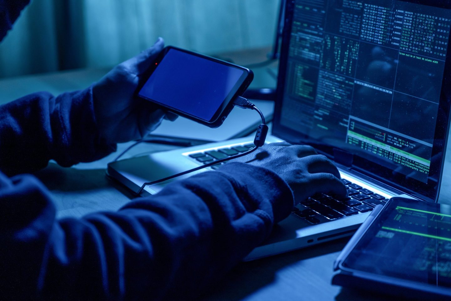Hacker with mobile phone and computer in a dark room