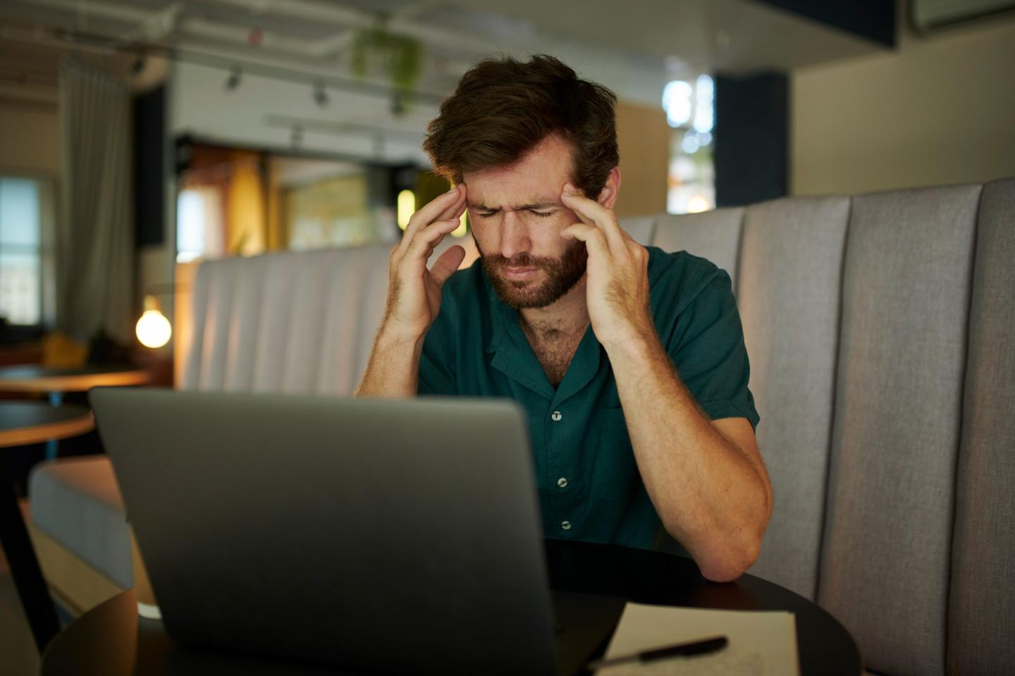 businessman with laptop in office, holding his temples in pain