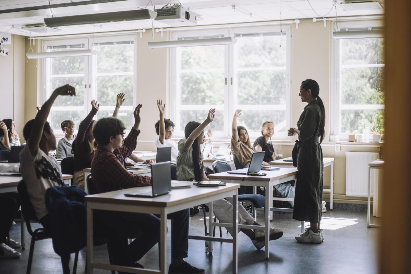 Students raising hands while teacher asking questions in class at school